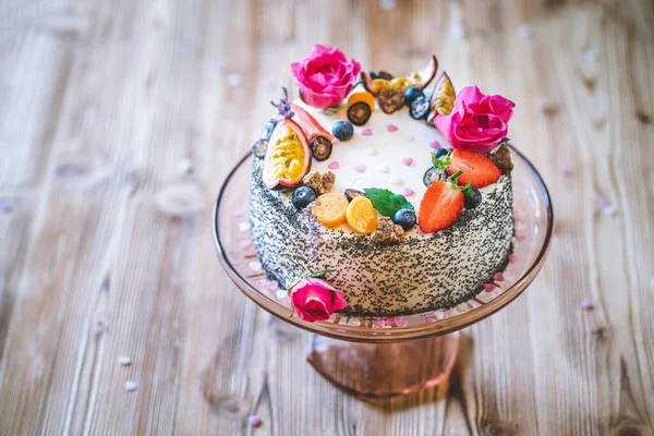 Taze meyveli tatlı beyaz cheesecake turtası ahşap masa arkasında haşhaş ve gül çiçekleri. Doğum günü, Sevgililer Günü ve kutlama için ideal bir hediye.