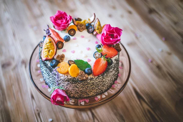 Taze meyveli tatlı beyaz cheesecake turtası ahşap masa arkasında haşhaş ve gül çiçekleri. Doğum günü, Sevgililer Günü ve kutlama için ideal bir hediye.