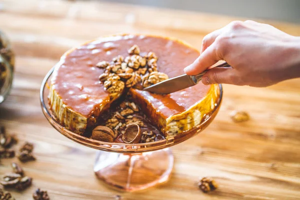 Kadın pastacılar el yapımı karamel kaplı chessecake ve ahşap masada ceviz fıstığı. Lezzetli kahverengi kek tatlısı.