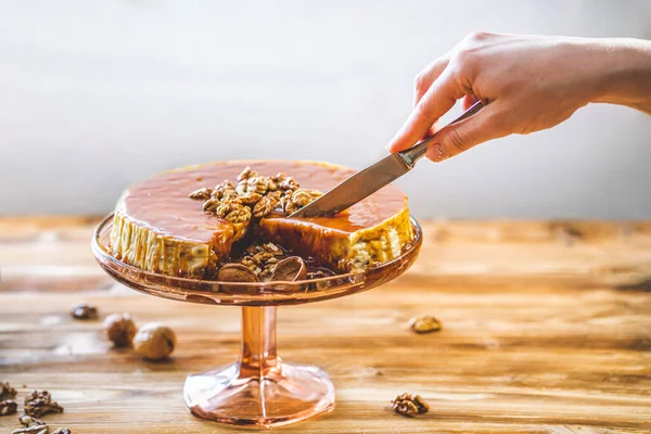 Kadın pastacılar el yapımı karamel kaplı chessecake ve ahşap masada ceviz fıstığı. Lezzetli kahverengi kek tatlısı.