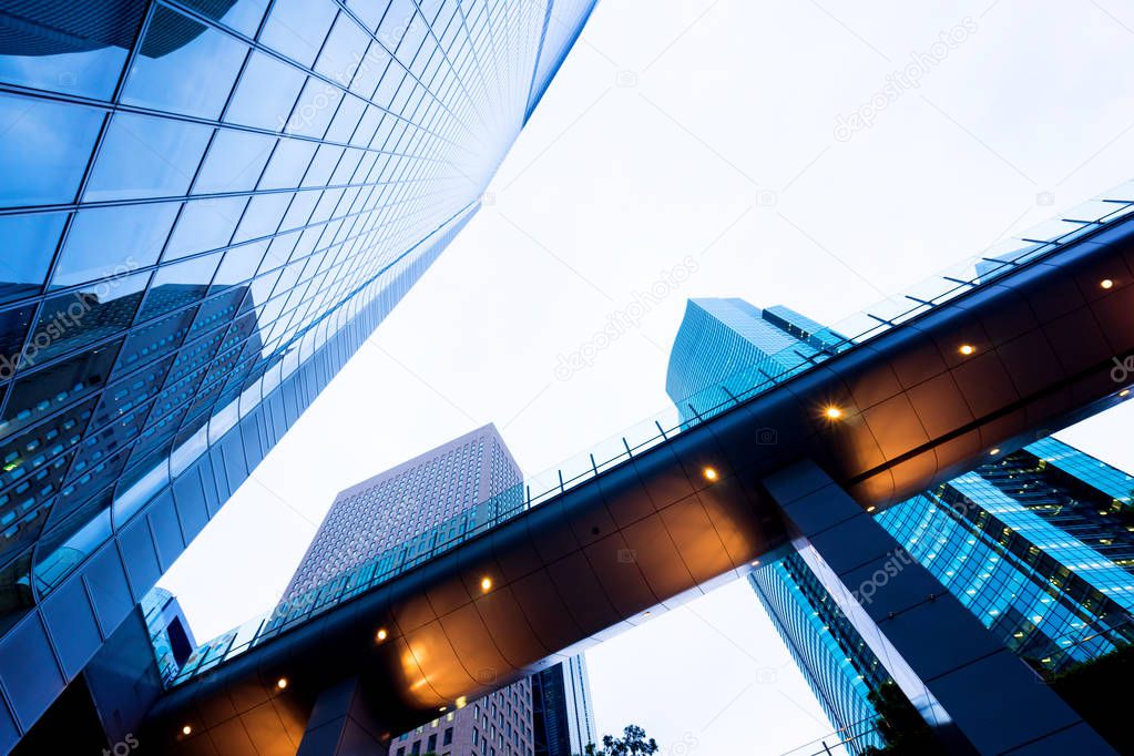 Business concept for real estate and corporate construction - looking up view in financial district, the silhouettes of skyscrapers city reflect dramatic blue sky, sun lights in Tokyo, Japan