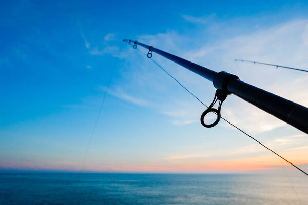 The silhouette of fishing poles under dramatic sunset and beautiful sea 