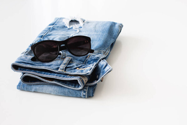 Jeans and sunglasses neatly folded on a white background 