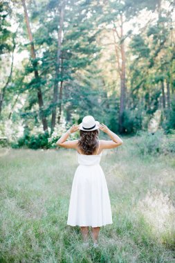 Beyaz elbiseli ve şapkalı bir kız. Sırtı doğaya dönük..