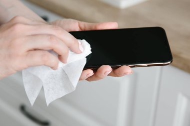 Bir kadın, grip ve Covid-19 enfeksiyonunu önlemek için cep telefonunu temizler ve dezenfekte eder..