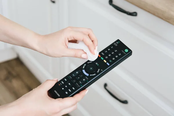 Kadın elleri yakın plan, uzaktan kumandayı pislikten temizler. Grip ve Covid-19 'un önlenmesi.