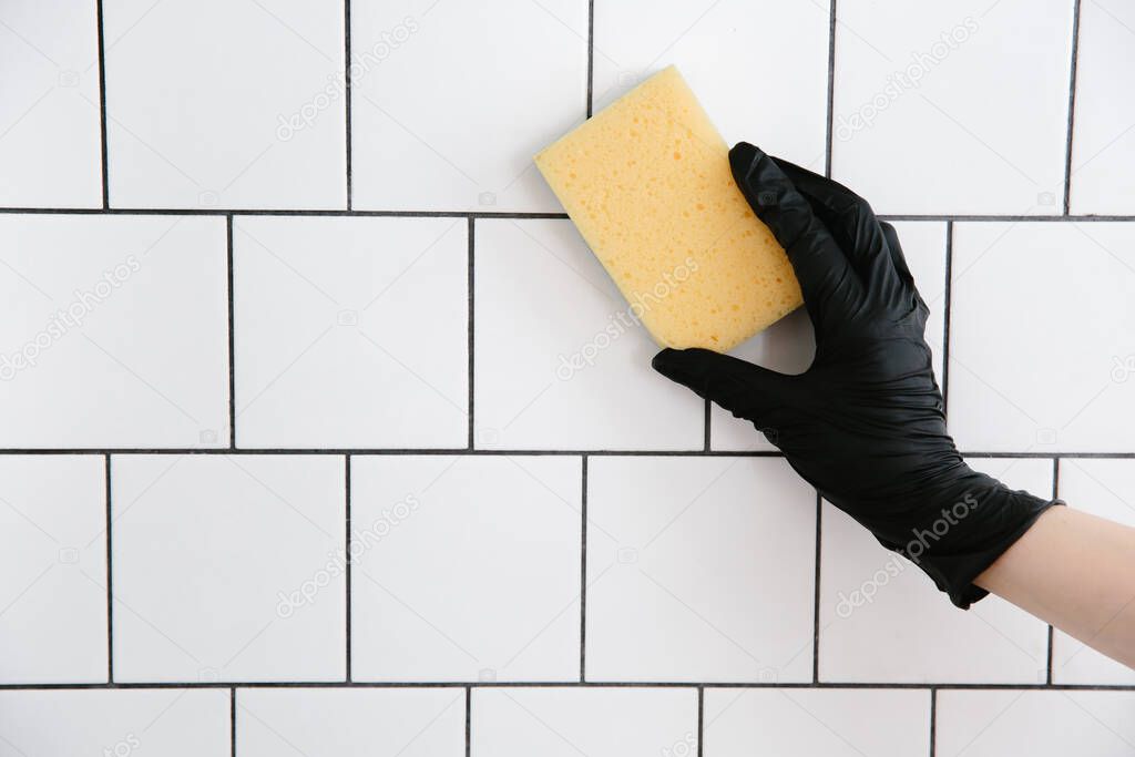 House cleaning, woman in black gloves washes with sponge white ceramic tile on the wall.