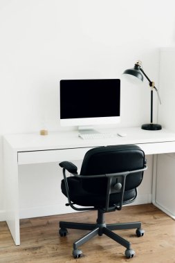 Siyah monitörü, masa lambası ve sandalyesi olan beyaz çalışma masası. İş yeri konsepti. İç mekanda minimalizm. Evden çalışmak, serbest çalışan işyeri..