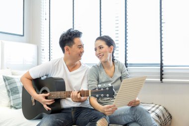 Genç çift modern yaşam konsepti için çağdaş evin yatak odasında birlikte gitar çalmak