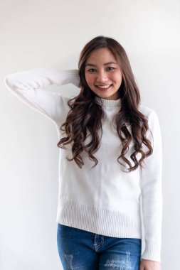 Kış için beyaz kazak giyen güzel Asyalı genç bir kızın portresi beyaz arka plandaki boş fotokopi alanını işaret ediyor.