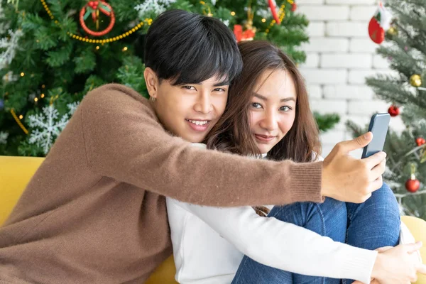 若いアジアの10代のカップルは クリスマスツリーの装飾とリビングルームで一緒にクリスマス休暇を祝うために彼らの自撮り写真を作る — ストック写真