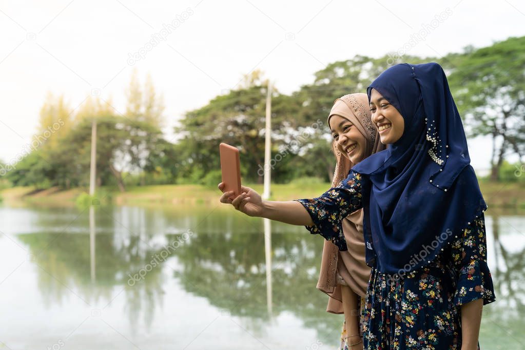 Young adult teenager Muslim Islamic Thai Asian women university students using smartphones to make their selfie photographing