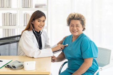 Doktor, hastane kliniğindeki muayene odasında steteskopla yaşlı kadınların nefesini dinliyor..