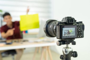 Genç Asyalı erkek çevrimiçi tüccar blogcu renkli alışveriş çantasıyla canlı video kaydediyor. Satışa hazırlanıyor ve malları evde gözden geçiriyor. Çevrimiçi sosyal medya kavramı. Kameraya odaklan.