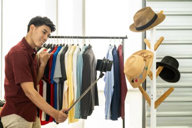 Genç Asyalı erkek çevrimiçi moda blogcusu günlük kıyafetleri incelemek için canlı video kaydı için akıllı cep telefonu kullanıyor. Sosyal medya kavramında çevrimiçi influcencer.