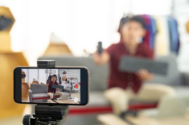 Genç Asyalı erkek çevrimiçi ticari blogcu akıllı cep telefonu kullanarak canlı video kaydı yapıyor. Ürün ürünlerini gözden geçirmek için. Çevrimiçi sosyal medya kavramı. Cep telefonuna odaklan