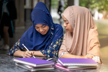 Teenager Young Adult Asian Thai Muslim university college students reading book and using digital tablet together using for education and online education concept clipart