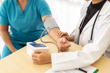 Hastane kliniğindeki muayene odasında yaşlı bir kadının tansiyonunu ölçen kadın doktor..