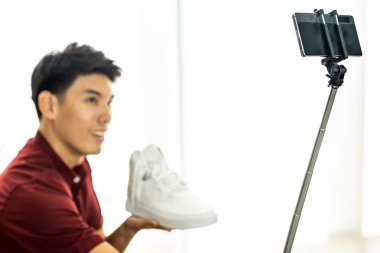 Genç Asyalı erkek çevrimiçi moda blogcusu günlük kıyafetleri incelemek için canlı video kaydı için akıllı cep telefonu kullanıyor. Çevrimiçi sosyal medya kavramı. Cep telefonuna odaklan