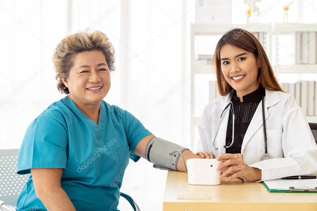 Female doctor measuring blood pressure of senior woman elderly at examination room in hospital clinic.