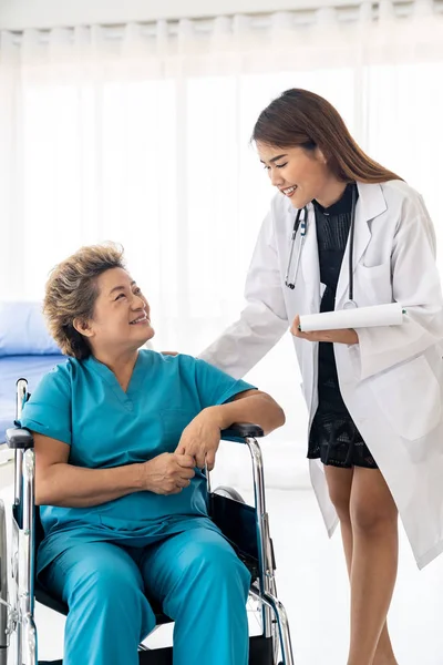 亚洲信心医生护理人员与坐在病房轮椅上接受日常检查的老年妇女谈论健康问题 — 图库照片