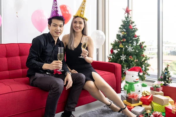 大都市の大きなマンションのリビングルームで一緒に輝くワインと一緒に新年のクリスマスの休日を祝う若いアジアの大人のカップル — ストック写真