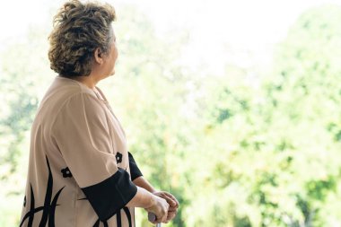 Yaşlı yaşlı bir kadın oturma odasındaki pencerenin yanında baston ya da baston kullanıyor - iyileşme ve rehabilitasyon konsepti