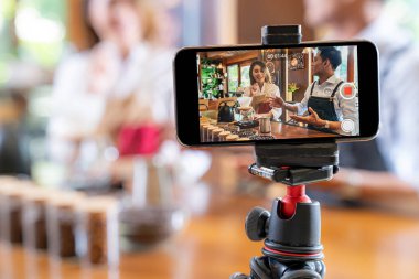 Genç yetişkin Asyalı girişimci kafe kahve dükkanının video bloğu ve kafedeki akıllı telefonuyla çevrimiçi pazarlama için sosyal medyada yaşıyor. Küçük işletme oluşturma ve tüketim kavramının başlangıcı için kullanılacak. 