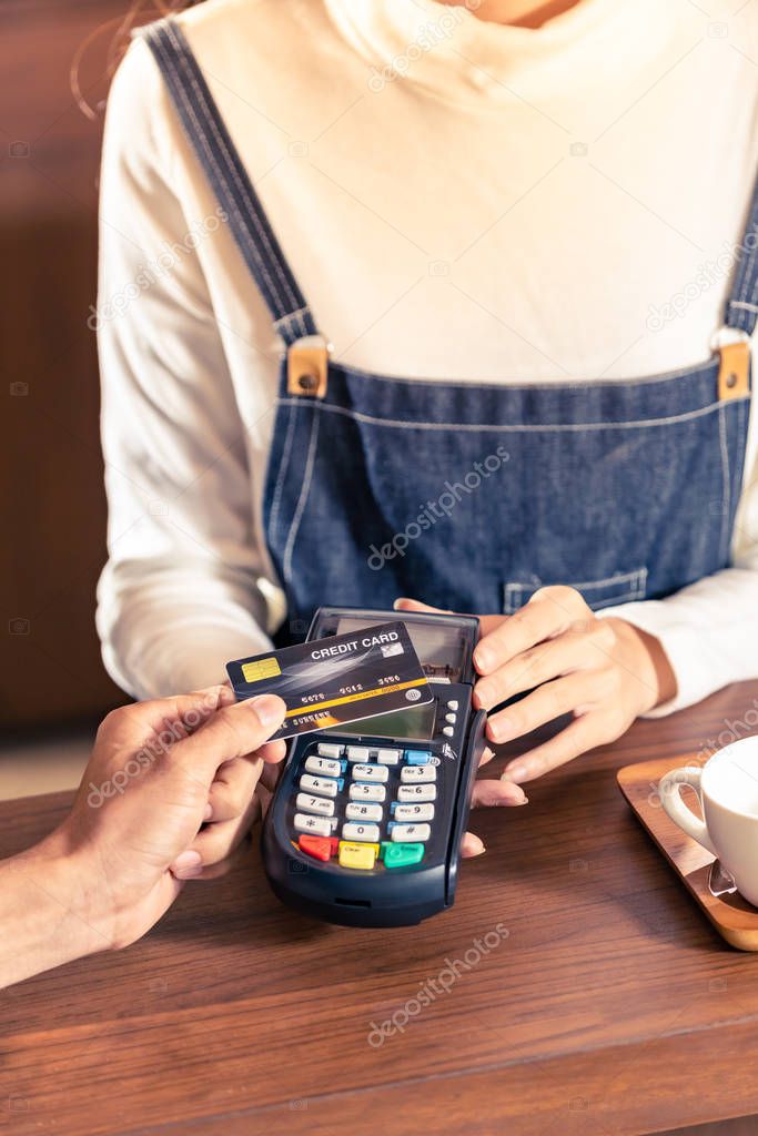 Close-up of asian customer using his credit card with contactless nfs technology to pay a barista for his coffee purchase at a cafe bar.