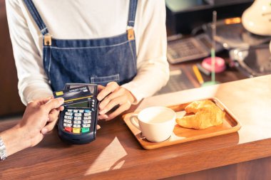 Asyalı müşterinin, bir kafe bardaki kahveciye parasını ödemek için bağlantısız NFS teknolojisiyle kredi kartını kullanması..