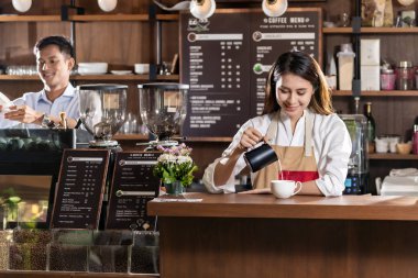 Kafe barında müşteriye kahve hazırlamak için taze süt dolduran Asyalı genç bayan barmen..
