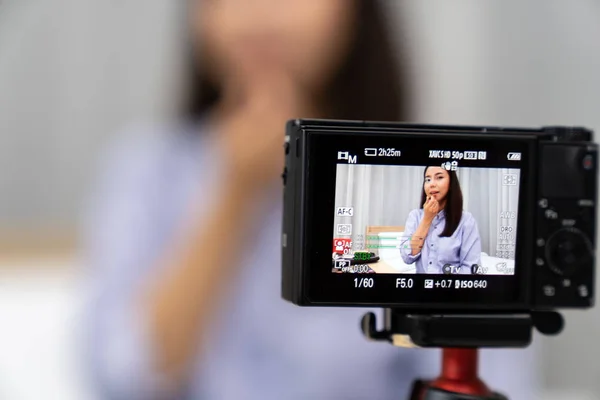 Young beautiful Asian woman beauty vlogger or blogger recording live how to make up tutorial to share on social media using digital camera on table tripod. Using for vlog social media influencer concept. Focus on camera.