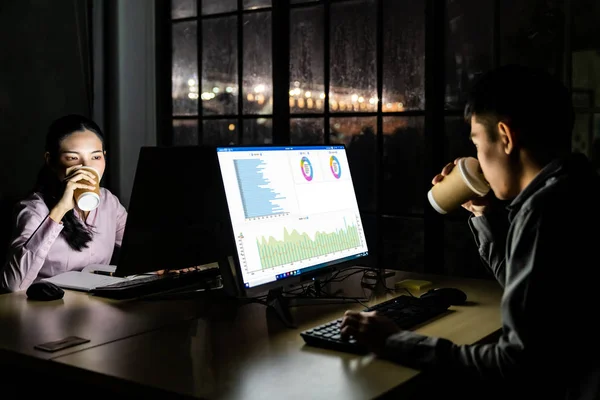 若い大人のアジアのビジネスマンや女性は デスクトップコンピュータやラップトップでオフィスで夜遅くまで働いている間にホットコーヒーを飲んでいます ハードワークや作業後期のコンセプトとして使用する — ストック写真
