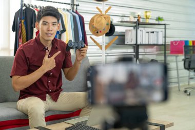 Genç Asyalı erkek çevrimiçi blogger oyun amaçlı oyun ürünleri için joystick 'i incelemek için canlı video kaydediyor. Çevrimiçi sosyal medya kavramı. Cep telefonuna odaklan