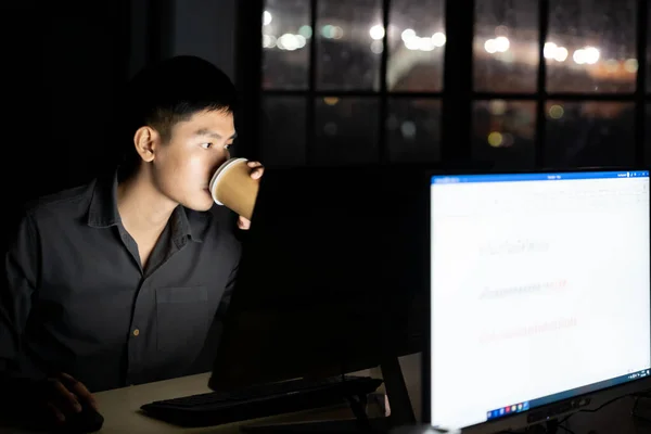 年轻的亚洲商人在工作到深夜的时候 在办公室里用台式计算机喝着热咖啡 采用努力工作和工作到深夜的概念 — 图库照片