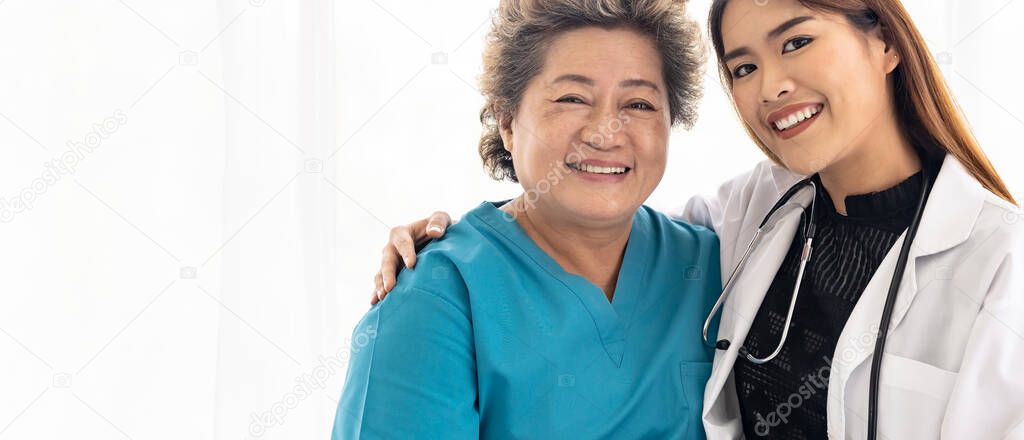 Young female doctor in uniform hugging and smiling to old elderly woman patient during a visit in hospital ward. Web banner Panorama crop.