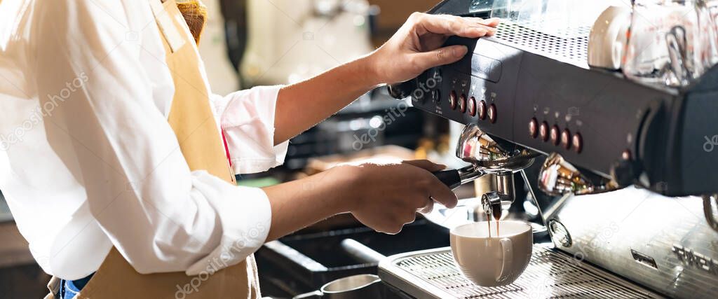 Close-up shot of a barista brewing coffee by modern coffeemaker machine to making a cup of coffee with other barista working. Using for small business entrepreneur owner, Panorama web banner crop.