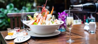 Panoramik web pankartı garsonu şarap kadehine beyaz şarap dolduruyor ve arka planda buzlu büyük kase deniz ürünleriyle restoranda müşterilere servis yapıyor. Restoran gastronomisi gıda ve içecek tüketim kavramı.