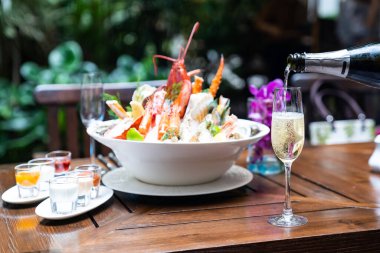 Garson şarap bardağına beyaz şarap dolduruyor ve arka planda buzlu büyük kase deniz ürünleriyle restoranda müşterilere servis yapıyor. Restoran gastronomisi gıda ve içecek tüketim kavramı.