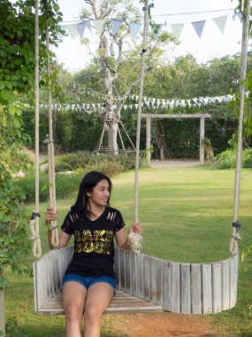 Asyalı kadın parkta ahşap salıncak üzerinde oturan