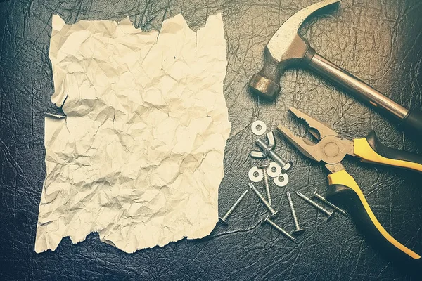 Boş, babalar gününde bir adamı tebrik etmek için bir form. Bir çekiç, pense ve cıvatalarla çevrili siyah bir arkaplan üzerine yazı yazmak için buruşmuş bir kağıt parçası.