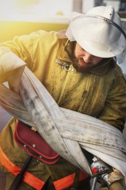 Kasklı sakallı bir itfaiyeci yangın hortumunu kıvırıyor. Yangın söndürme bitti..