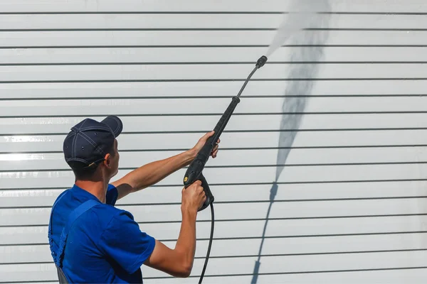 Worker in overalls washes a white wall from a siding with a water gun — Stock Photo, Image