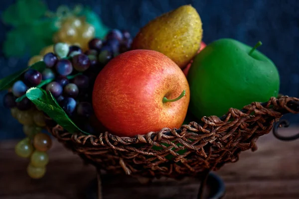 Artificial fruits lie in a wicker basket. Still life with dark lighting. Background. — Stock Photo, Image