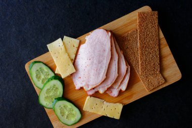 Ahşap bir tahtada et, salatalık, peynir ve lanet olası ekmekleri dilimlemek. Yukarıdan bir bakış. Taze ve sulu kahvaltı veya atıştırmalık