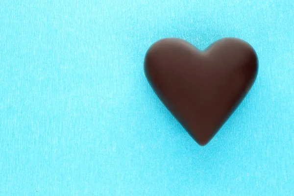 Mavi arka plan üzerinde siyah çikolata kalp — Stok fotoğraf