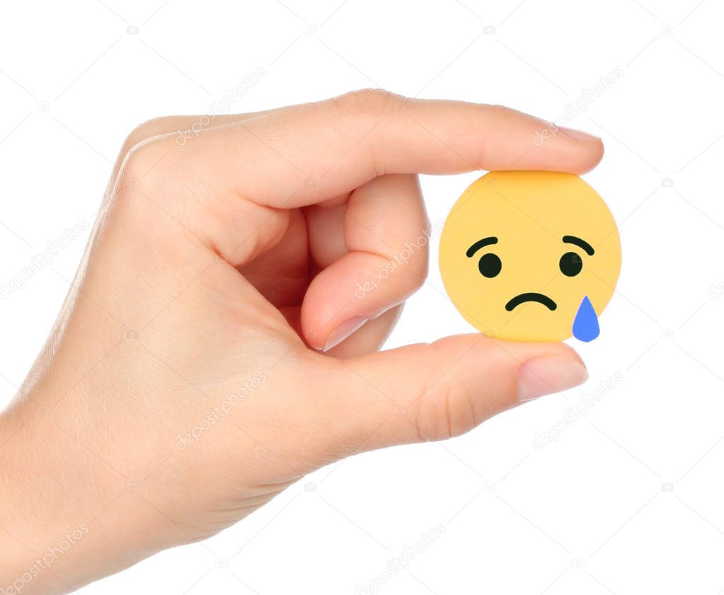 Kiev, Ukraine - September 04, 2017: Hand holds Facebook Sad Empathetic Emoji Reaction, printed on paper. Facebook is a well-known social networking service
