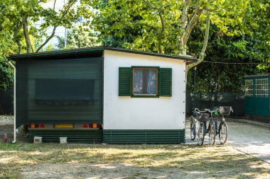 Kamp alanındaki küçük beyaz bungalov. Bungalovun önünde bisikletler. 