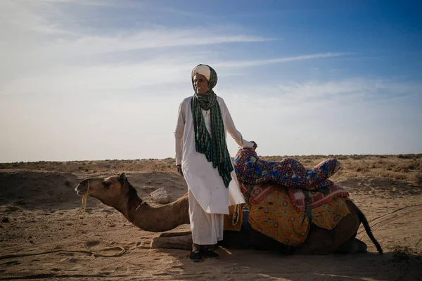 Человек, стоящий рядом с верблюдом в пустыне — стоковое фото
