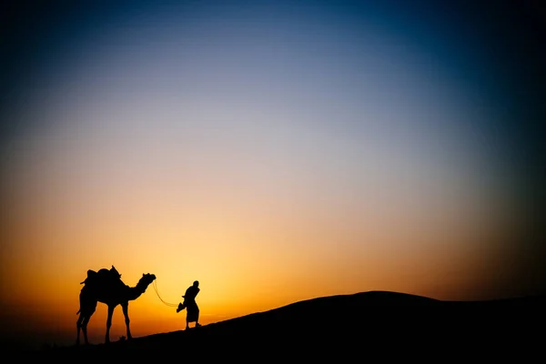 Силуэт человека и верблюда в пустыне — стоковое фото